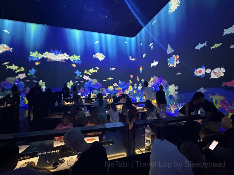 絵を描く人々とディスプレイ中を泳ぐ魚たち